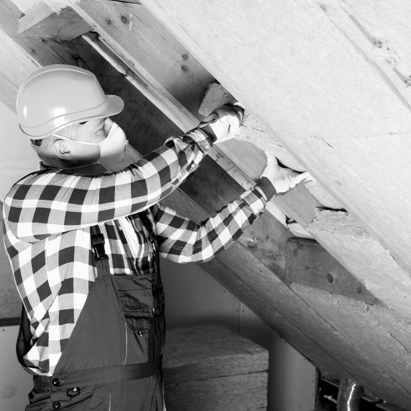Black and white photo of a man in protective gear removing insulation.