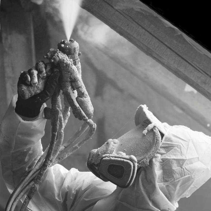 Black and white photo of a person in protective gear spraying insulation.