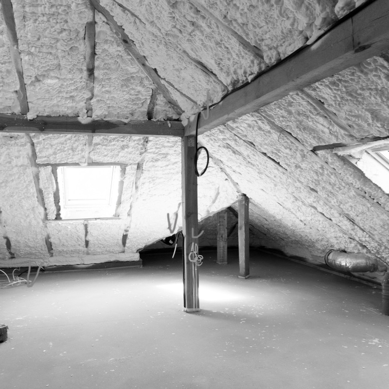 Black and white photo of spray fibre insulation in an attic.